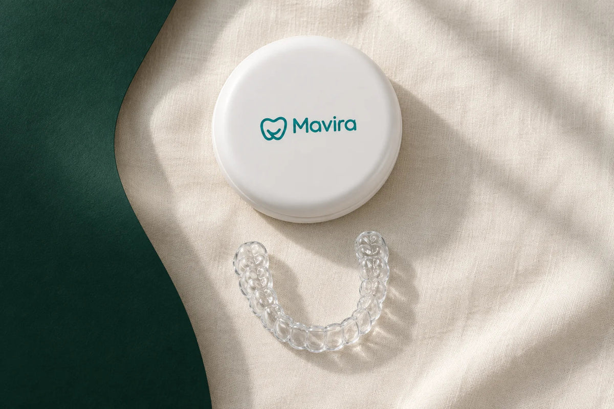 White Mavira case and a clear retainer on ivory linen beside a deep green backdrop.